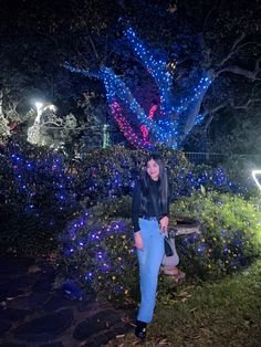 a woman standing in front of a tree with blue lights on it at night time