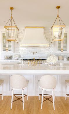 a large kitchen with white cabinets and gold accents on the hood over the stove is surrounded by three stools