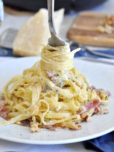 a fork is stuck into some pasta on a plate with other food items in the background