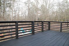 a wooden deck with black railings and trees in the backgroung area