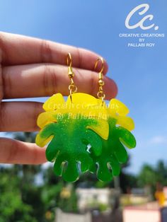 a hand holding a yellow and green flower shaped keychain in front of a blue sky