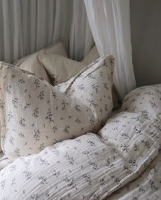 an unmade bed with two pillows and white drapes on the window sill