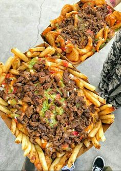 two trays filled with different types of food sitting on top of each other next to someone's feet