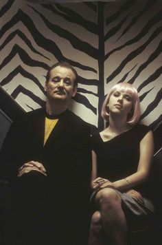 a man and woman sitting next to each other in front of a zebra print wall