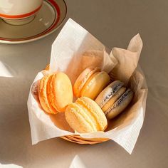 a basket filled with assorted macaroons next to a cup of coffee