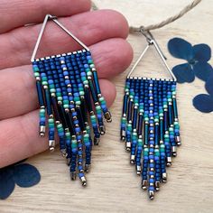 a pair of blue and green beaded earrings on a wooden table with flowers in the background