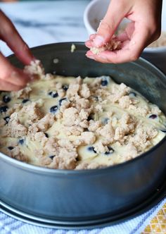 two hands reaching for food in a metal bowl on a blue and white table cloth