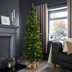 a living room with a christmas tree next to a couch and fireplace in front of a window