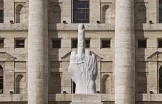 a large white hand statue in front of a building with columns and arches on both sides