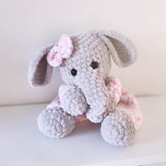 a small crocheted elephant with a pink bow on its head sitting on a shelf