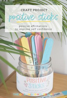 a jar filled with colorful wooden sticks sitting on top of a table next to a plant