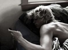 a shirtless man laying on top of a bed holding a cell phone in his hand