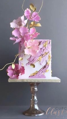 a white and pink cake with gold leaf decorations on the top is sitting on a silver pedestal