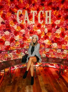 a woman sitting on top of a bench in front of a floral wall with the word catch