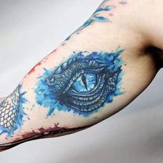 a man's arm with watercolor tattoos and an all seeing eye on it