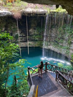 a woman is standing at the top of stairs looking out over a pool and waterfall