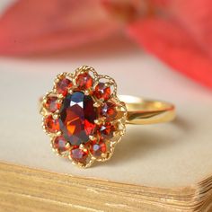 A delightful vintage English, halo-style dress ring, cluster-set with natural garnet. Measuring 7x5mm (0.75ct), the central oval garnet is surrounded by a halo of 10 round-cut garnets totalling approximately 0.30ct. Crafted from 9ct yellow gold, the face of the ring is encircled by a fine twisted wire-work frame, completing the impression of a lacey-edged flower head. Sweet, colourful and so very cheerful! The perfect accessory for a vintage spring outfit. This ring is a size N (AU/UK) or 6 3/4 Heirloom Oval Garnet Cluster Ring, Vintage Cluster Ring With Halo Design, Vintage Gold Ring With Halo, Vintage Oval Cluster Ring With Gemstone, Vintage Yellow Gold Cluster Ring With Halo Design, Vintage Red Garnet Cluster Ring, Vintage Halo Cluster Ring Gift, Vintage Cluster Ring With Halo As Gift, Vintage Oval Ruby Ring With Halo Setting