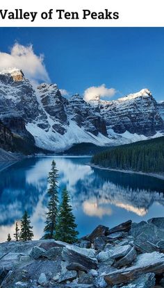 the mountains are covered in snow and there is a lake surrounded by rocks, pine trees and boulders