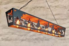 a wooden light hanging from a chain with lights on it's sides and silhouettes of people riding horses