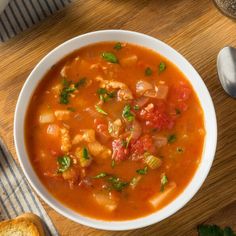 a bowl of soup on a wooden table with bread and spoons next to it