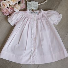 This Feltman Brother's Newborn Dress/Gown Is Simply Beautiful! The All Pink Dress Is Done In A Cotton Blend For Easy Care. The Neckline Is Smocked In A Honeycomb Design With White Embroidery. A Delicate White French Lace Trims The Neck. The Front Of The Gown Has A Button Placket And Is Trimmed On Each Side With A Matching Lace. Sweet White Flowers With Pink Centers, Along With A White Vine, Is Hand-Embroidered At The Top Of The Button Placket. The Short Puff Sleeves Gather With Elastic And Have Fitted Smock Baptism Dress For Spring, Pink Fitted Smocked Dress For Baptism, Newborn Girl Dresses, Kids Christmas Dress, Hand Smocked Dress, Girl Red Dress, Heirloom Dresses, Cheerleading Outfits, Green Floral Dress