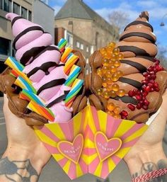 two ice cream cones with chocolate and candy toppings in their hands, on the street