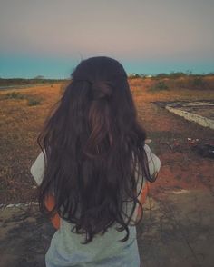 the back of a woman's head with long dark hair in an open field