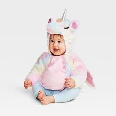 a baby sitting on the floor wearing a unicorn costume and smiling at the camera with her hands in her pockets