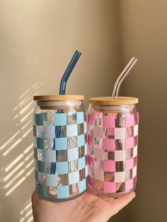 two colorful jars with straws in them are being held by someone's hand