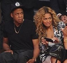 a man and woman sitting next to each other at a basketball game, one holding a cell phone