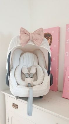 a baby's car seat with a pink bow on it and two paintings behind it