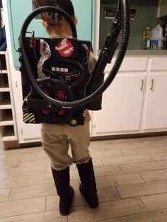 a young boy is standing in the kitchen with a vacuum and hose attached to his back