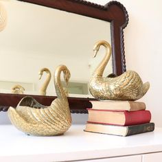 two golden swans sitting on top of books in front of a mirror