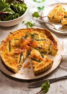 a quiche with salmon and spinach is on a plate next to a salad