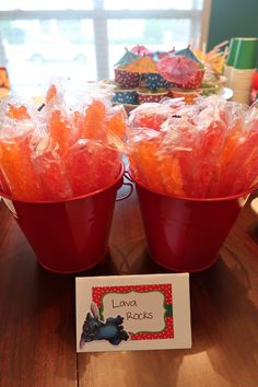 two red buckets filled with candy sitting on top of a table next to a card