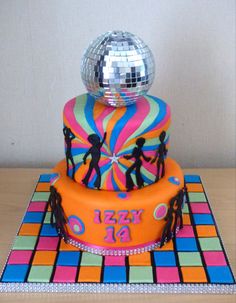 a colorful cake with disco balls and people on the top is sitting on a table