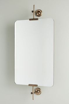 a mirror mounted to the wall with two brass hooks on it's back side