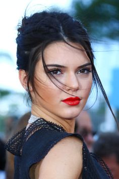 a woman with dark hair and red lipstick wearing a black dress at an outdoor event