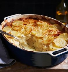 a blue casserole dish with potatoes in it and a spoon on the side