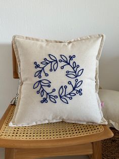 a white pillow with blue embroidery on it sitting on a wooden chair next to a wicker basket