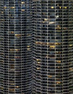 an aerial view of some very tall buildings in the city at night with lights on