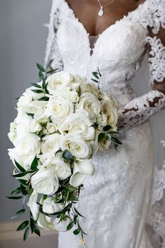 a bride holding a bouquet of white roses and greenery on her wedding day,