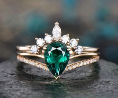 an emerald colored ring with white diamonds on top and gold band, sitting on a rock