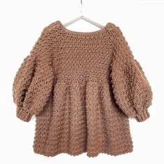 a crocheted sweater hanging on a hanger with the back turned to show it's long sleeves