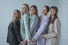 four women standing in front of a white tiled wall with their hands on their hips