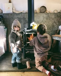 two young boys standing in front of an open wood burning stove with their feet on the floor