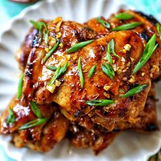 two pieces of chicken on a white plate with green garnish and sesame seeds