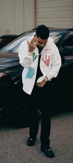 a man standing in front of a black car talking on a cell phone while holding his hand up to his ear