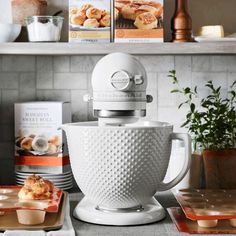 a white mixer sitting on top of a counter next to some plates and food items