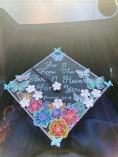 a decorated graduation cap sitting on top of a car trunk with butterflies and flowers all over it